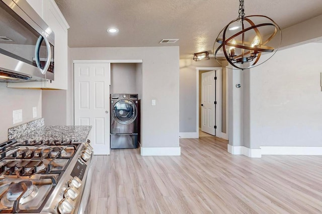 kitchen featuring light stone counters, white cabinets, light hardwood / wood-style flooring, washer / clothes dryer, and appliances with stainless steel finishes