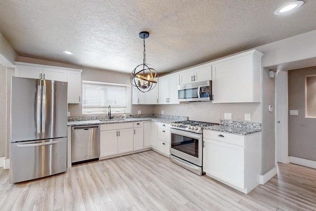 1139 Forrester Ave NW, Albuquerque, NM 87104 - kitchen with light wood finished floors, an inviting chandelier, a sink, white cabinets, and appliances with stainless steel finishes