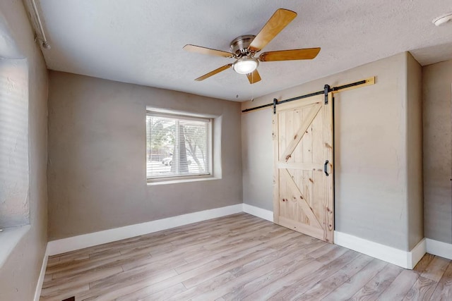 1139 Forrester Ave NW, Albuquerque, NM 87104 - unfurnished room featuring a textured ceiling, a barn door, a ceiling fan, baseboards, and light wood-style floors