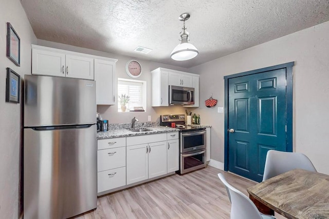 kitchen with appliances with stainless steel finishes, hanging light fixtures, light hardwood / wood-style floors, and white cabinets