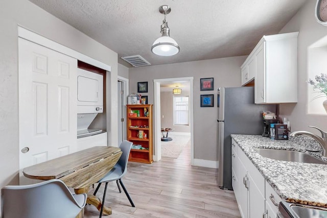 kitchen featuring light wood-type flooring, stacked washer and clothes dryer, sink, light stone countertops, and white cabinets