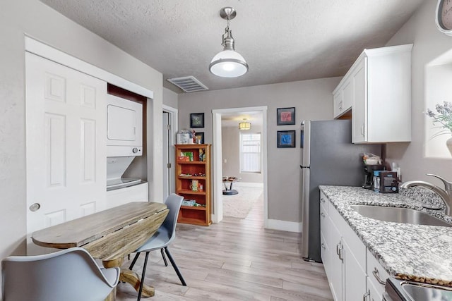 1139 Forrester Ave NW, Albuquerque, NM 87104 - kitchen with a sink, visible vents, stacked washer and clothes dryer, white cabinetry, and light wood-style flooring