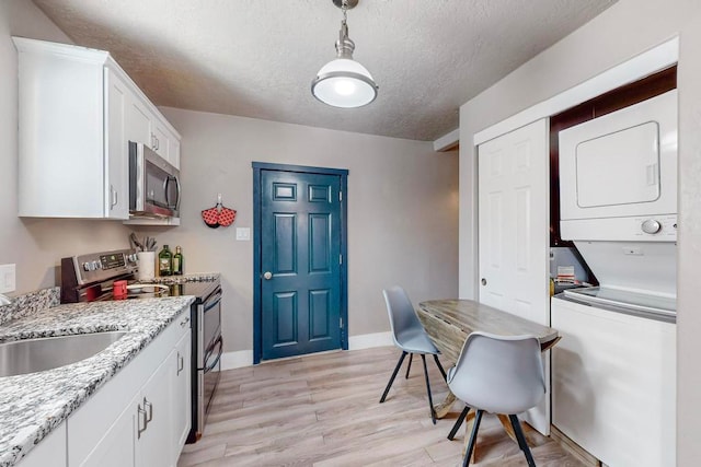 kitchen with light stone countertops, stacked washer and dryer, light hardwood / wood-style floors, white cabinetry, and appliances with stainless steel finishes