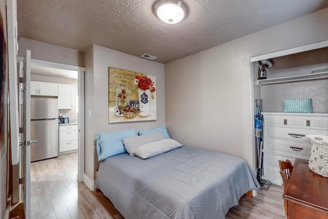 bedroom featuring a textured ceiling, stainless steel refrigerator, and light hardwood / wood-style flooring