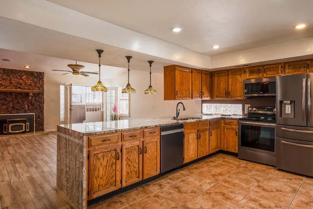 kitchen featuring light stone counters, sink, kitchen peninsula, decorative light fixtures, and stainless steel appliances