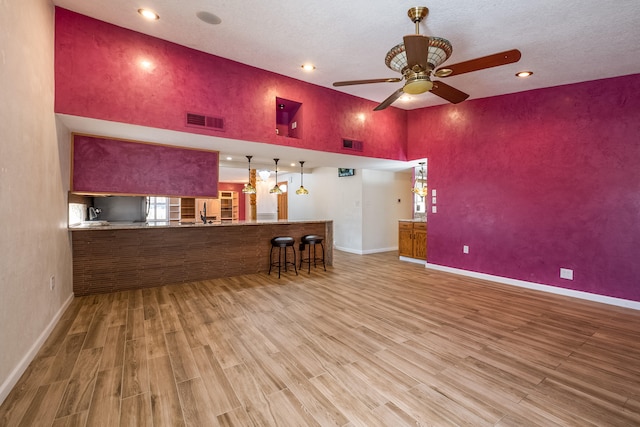 bar with ceiling fan, hanging light fixtures, a towering ceiling, light hardwood / wood-style flooring, and a textured ceiling