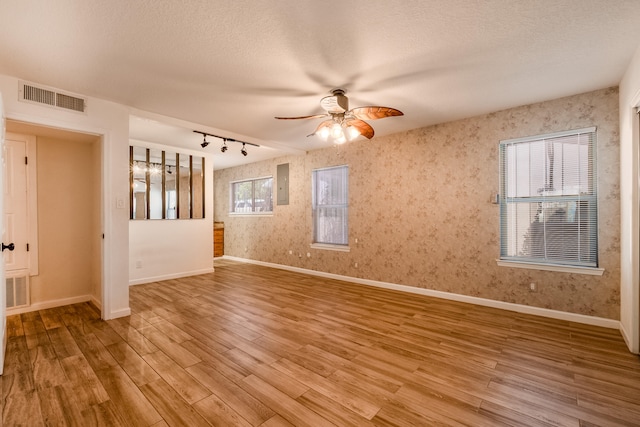 spare room featuring light wood-type flooring, ceiling fan, rail lighting, and a textured ceiling