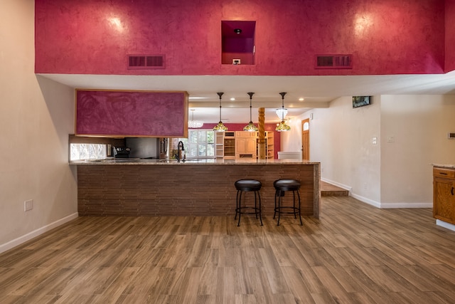 bar with hardwood / wood-style flooring, sink, hanging light fixtures, and a towering ceiling