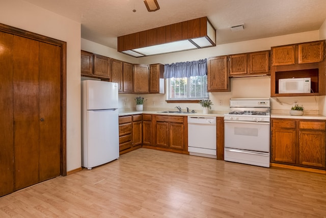 kitchen with light wood-type flooring, white appliances, sink, and a textured ceiling