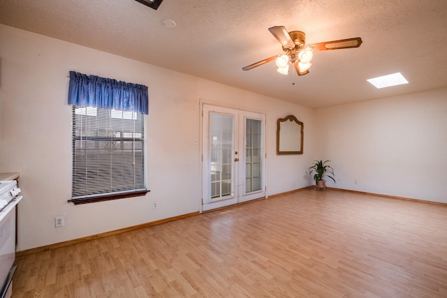 empty room featuring a skylight, ceiling fan, light hardwood / wood-style floors, and a textured ceiling