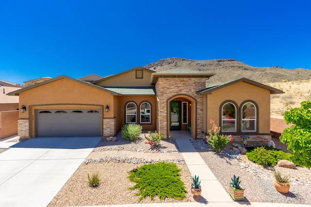 mediterranean / spanish house with stucco siding, stone siding, a mountain view, concrete driveway, and an attached garage