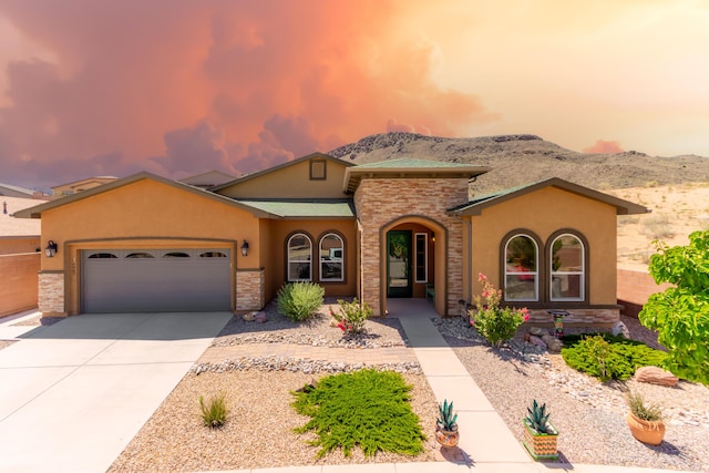 mediterranean / spanish home featuring a garage, a mountain view, driveway, stone siding, and stucco siding