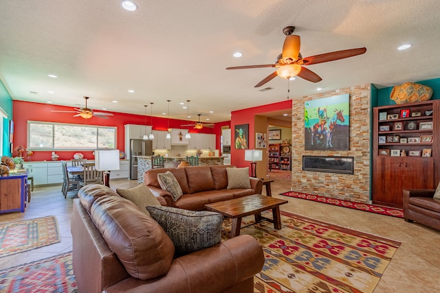 tiled living room featuring ceiling fan, a textured ceiling, and a fireplace