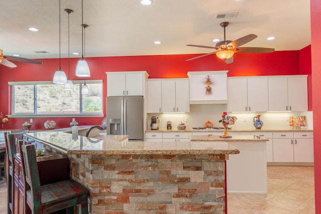 kitchen featuring a breakfast bar area, visible vents, a large island with sink, a ceiling fan, and stainless steel fridge with ice dispenser