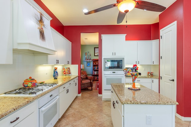 kitchen with white cabinets, light stone countertops, a kitchen island, and white appliances