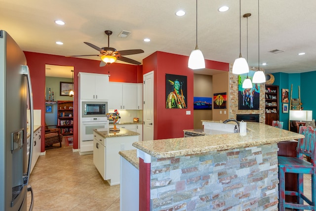 kitchen featuring white oven, hanging light fixtures, an island with sink, white cabinetry, and stainless steel refrigerator with ice dispenser