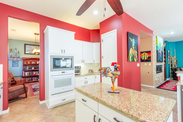 kitchen with light tile patterned flooring, ceiling fan, white cabinetry, and light stone countertops