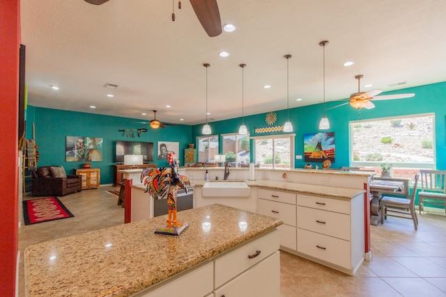 kitchen featuring light stone countertops, sink, a large island, pendant lighting, and white cabinets