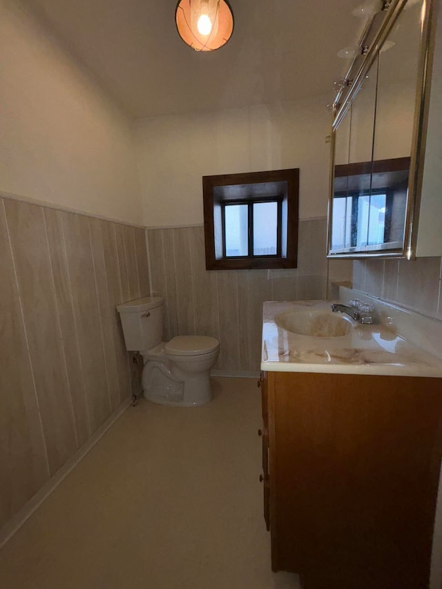 bathroom with wood walls, plenty of natural light, vanity, and toilet