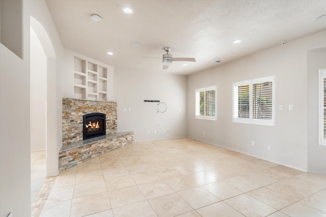 unfurnished living room featuring a fireplace, ceiling fan, built in features, and a textured ceiling