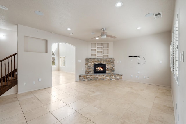 living room with a textured ceiling, ceiling fan, built in features, a fireplace, and light tile patterned flooring