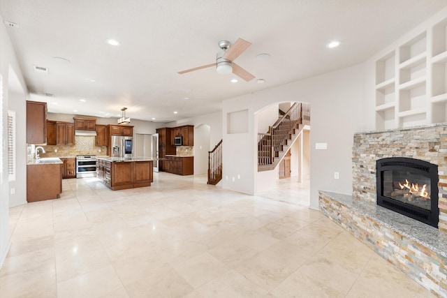 living room featuring built in shelves, ceiling fan, sink, a fireplace, and light tile patterned flooring