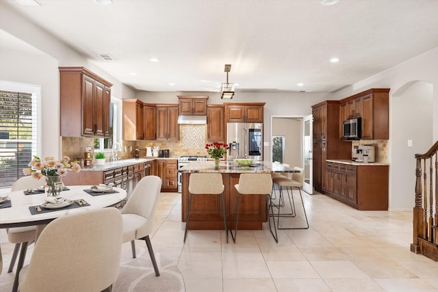 kitchen with light stone counters, backsplash, decorative light fixtures, a kitchen island, and appliances with stainless steel finishes