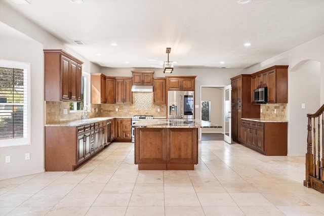 kitchen with light stone countertops, backsplash, decorative light fixtures, a kitchen island, and appliances with stainless steel finishes