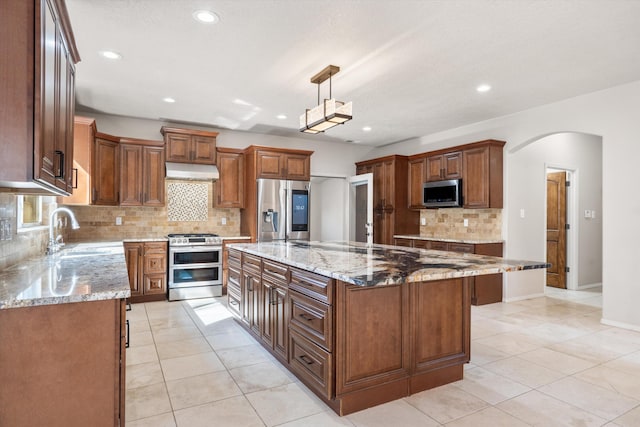 kitchen featuring light stone countertops, stainless steel appliances, sink, decorative light fixtures, and a center island