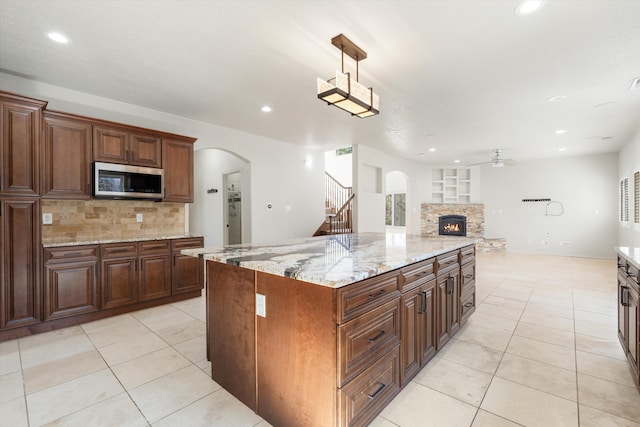 kitchen with a stone fireplace, a spacious island, hanging light fixtures, ceiling fan, and light tile patterned floors