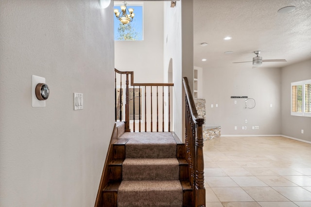 staircase featuring a textured ceiling, ceiling fan with notable chandelier, and tile patterned floors