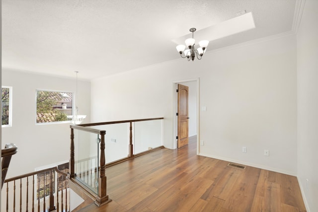 spare room featuring crown molding, wood-type flooring, a textured ceiling, and a chandelier