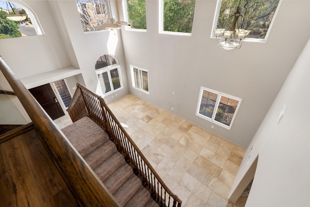 staircase with a towering ceiling, a healthy amount of sunlight, and a notable chandelier