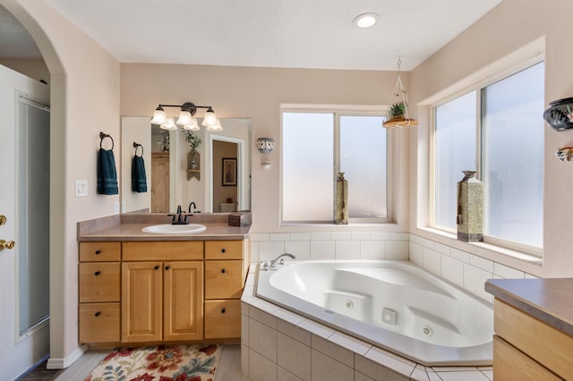 bathroom with vanity, tiled bath, and plenty of natural light