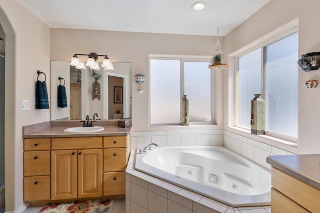 bathroom with a wealth of natural light, vanity, and a relaxing tiled tub