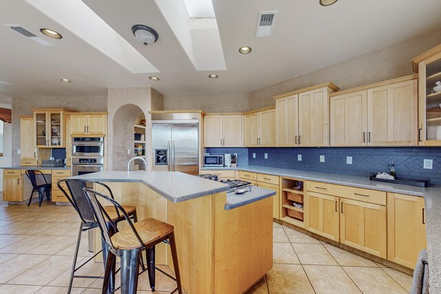 kitchen with appliances with stainless steel finishes, light brown cabinetry, light tile patterned floors, a breakfast bar area, and an island with sink