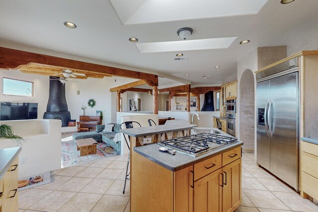 kitchen featuring a wood stove, a skylight, a center island, stainless steel appliances, and light tile patterned floors