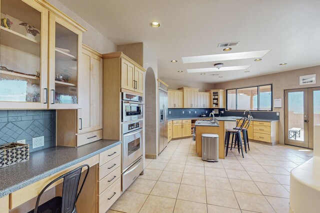 kitchen with a breakfast bar, a center island with sink, a skylight, tasteful backsplash, and stainless steel fridge with ice dispenser