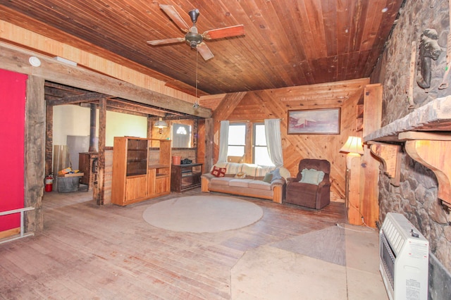 living room featuring ceiling fan, wood-type flooring, heating unit, wooden walls, and a wood stove