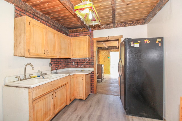 kitchen featuring black fridge, sink, light hardwood / wood-style floors, and brick wall