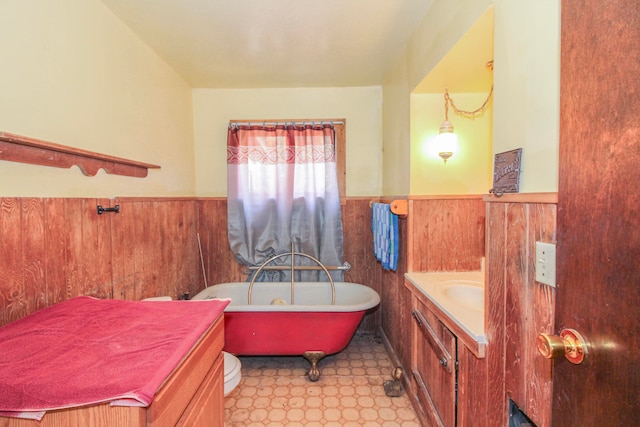 bathroom featuring vanity, a bathtub, wooden walls, and toilet