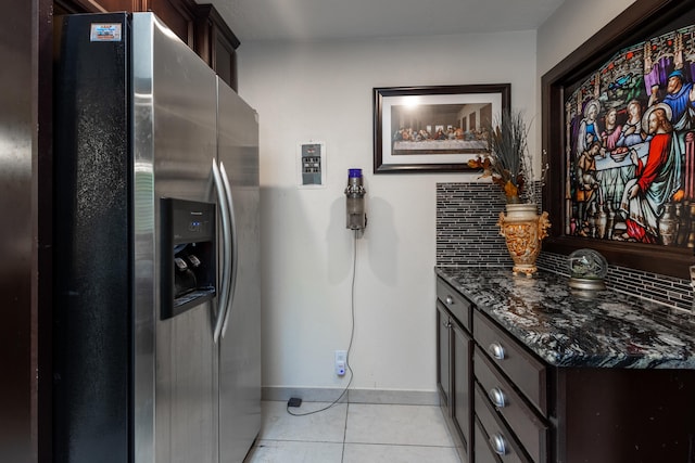 kitchen featuring dark brown cabinetry, stainless steel fridge, light tile patterned floors, tasteful backsplash, and dark stone counters