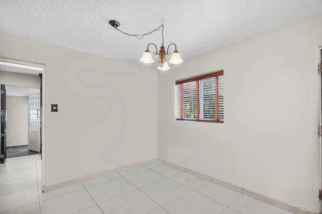 spare room featuring a chandelier, light tile patterned floors, and a textured ceiling