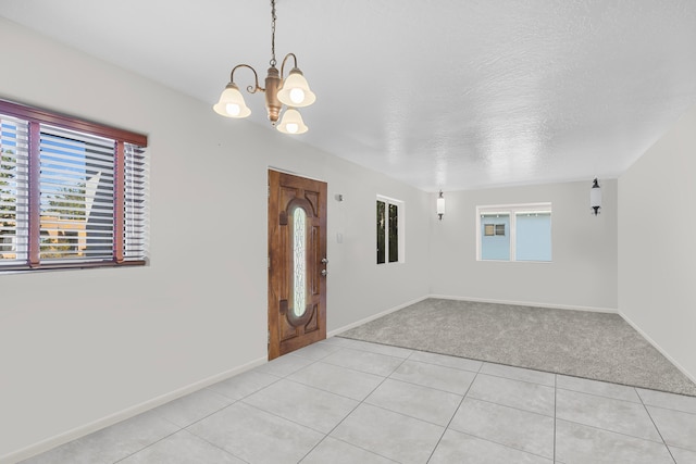 tiled spare room featuring an inviting chandelier, a textured ceiling, and a healthy amount of sunlight