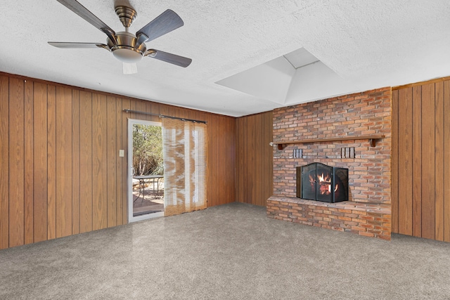 unfurnished living room with ceiling fan, a textured ceiling, a fireplace, and wood walls