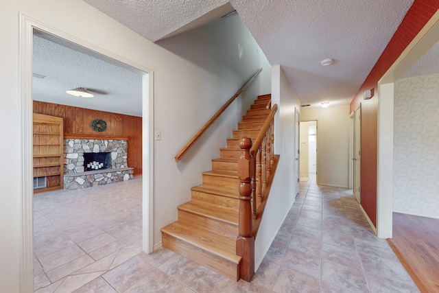 staircase with a stone fireplace, a textured ceiling, and wooden walls