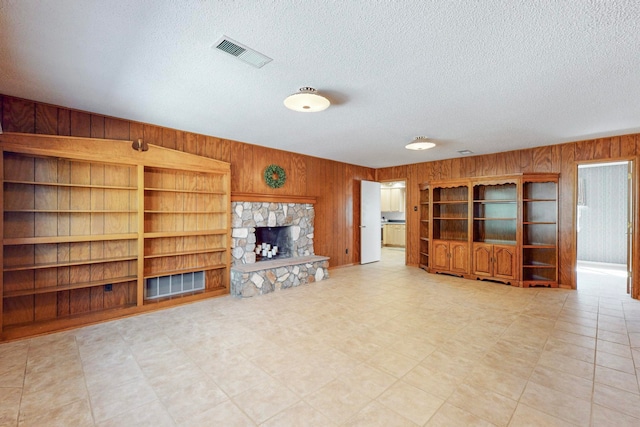 unfurnished living room featuring a fireplace, wooden walls, and a textured ceiling