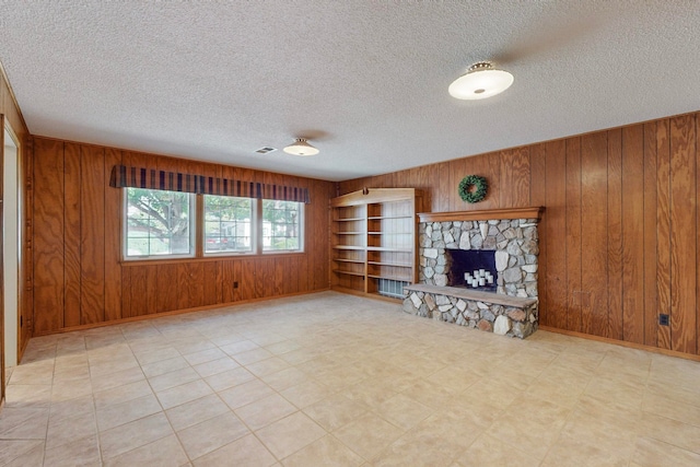 unfurnished living room with a stone fireplace, wooden walls, a textured ceiling, and built in shelves