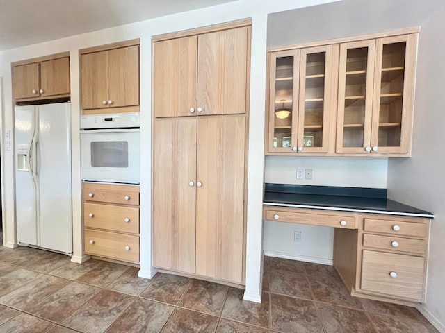 kitchen featuring light brown cabinets, built in desk, and white appliances