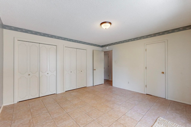 unfurnished bedroom with a textured ceiling, light tile patterned floors, and multiple closets